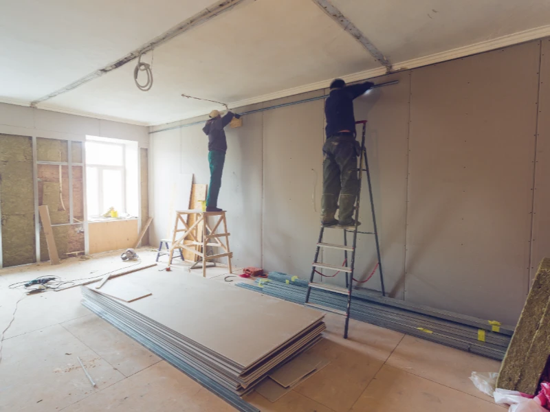 Two workers on ladders installing drywall in a room under construction. commercial water damage restoration