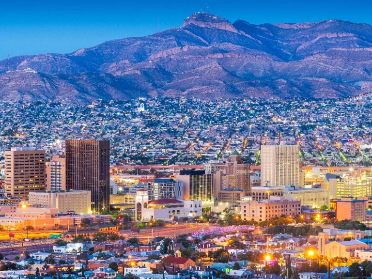 City skyline at dusk with illuminated buildings and mountains in the background. water damage restoration in El Paso