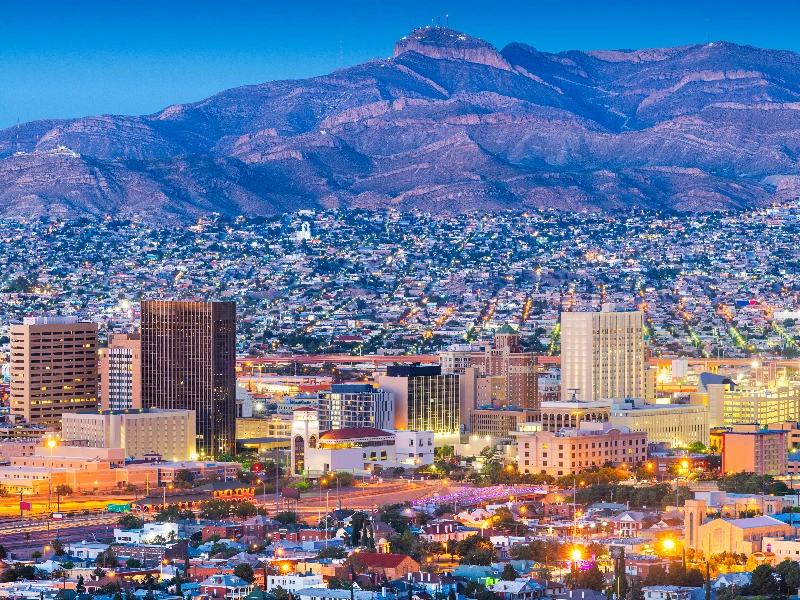 City skyline at dusk with illuminated buildings and mountains in the background. water damage restoration in El Paso