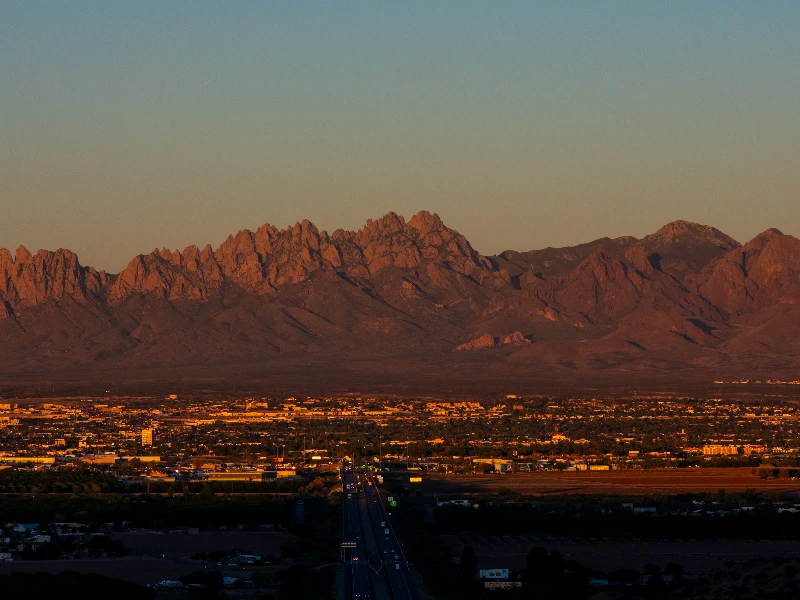 Sunset-lit cityscape with a mountain range in the background and a highway leading into the city. water damage restoration Las Cruces