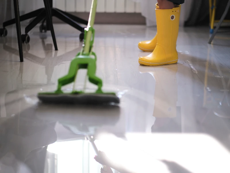 Person wearing yellow rain boots mopping a shiny floor with a green mop at a trusted restoration company
