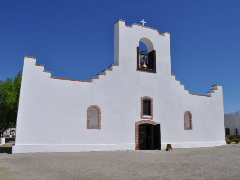 White adobe church with a bell tower and cross under a clear blue sky, water damage restoration in Socorro TX