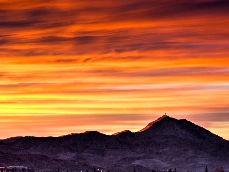 Mountain silhouette with a cross on the peak under a vibrant orange and yellow sunset sky. water damage restoration in Sunland Park