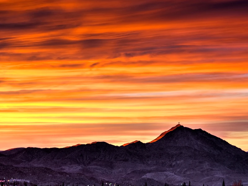 Mountain silhouette with a cross on the peak under a vibrant orange and yellow sunset sky. water damage restoration in Sunland Park