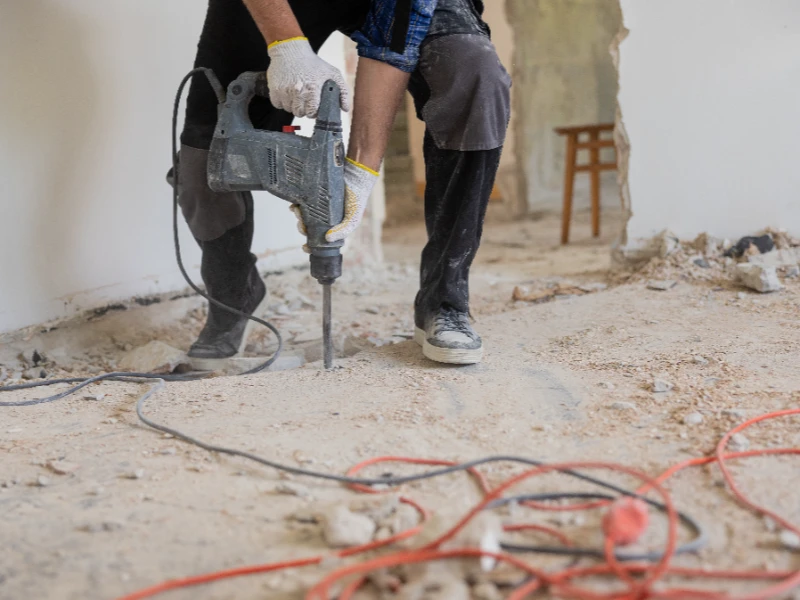 Worker using a jackhammer to break concrete floor inside a building under renovation. disaster reconstruction services